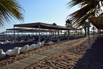 Path along the wooden decking on the beach to the sea between rows of sunbeds and pavilions in...