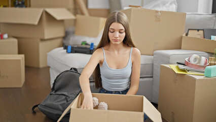 Fototapeta na wymiar Young beautiful girl unpacking cardboard box sitting on floor at new home