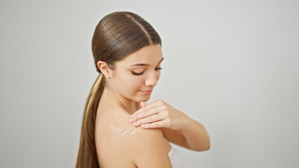 Young beautiful girl smiling confident applying skin lotion on shoulder over isolated white...