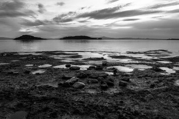 Shore of Trasimeno lake Umbria, Italy with rocks beneath a moody sky - 614541541