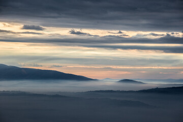 Mist and fog between valley and layers of mountains and hills at sunset, in Umbria Italy - 614541716