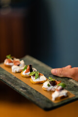 server's hand passing tray of basil, ricotta and prosciutto crostini