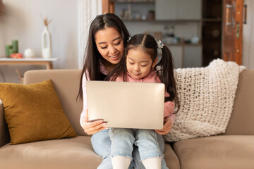 Young Asian Woman With Baby Daughter Using Laptop At Home