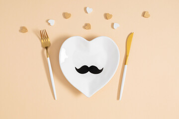 Father's Day concept. Flat lay top view of plate cutlery knife fork gift box, black mustache and hearts on pastel beige background with space for text or promotion and greeting message, banner