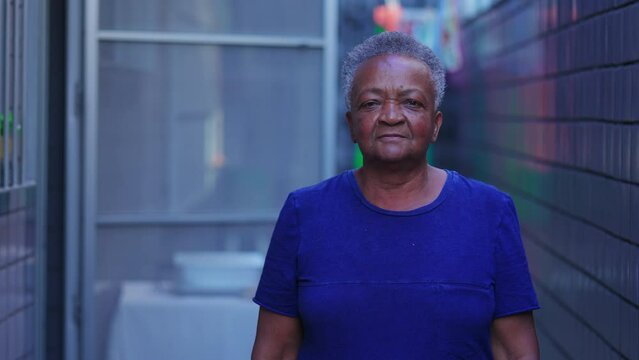 One black senior woman standing in residential patio outside looking at camera with neutral expression. African American elderly person in 70s