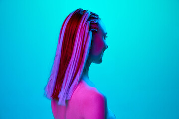 Side view portrait of young pretty girl with stylish hairstyle posing, looking straight against blue studio background in neon light. Concept of youth, emotions, beauty, lifestyle, ad