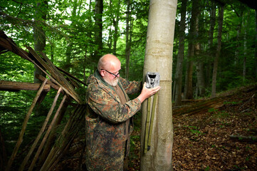 Hunter sets a trail camera on a tree in the forest. Trail cameras are often used by hunters for...