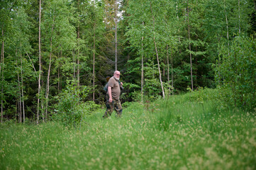 Senior hunter in a camouflage suit walking in the forest. Concept of travelling and hunting.