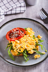 Bruschetta with scrambled egg, arugula, tomato and sesame on a plate vertical view