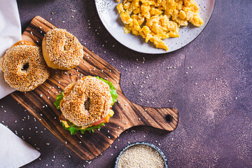 Homemade bagel with scramble egg, bacon, cheese, tomato and lettuce on a board top view