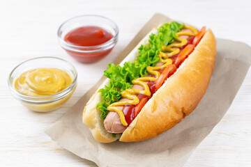 Homemade Hot Dog with yellow mustard, ketchup, tomato and fresh salad leaves on white wooden background. Fast food, street food, american cuisine