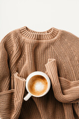 Brown knitted sweater with coffee cup on white background. Autumn or winter drink, hygge concept.