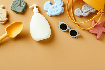 Flat lay silicone beach toys, sunglasses, hat, sunscreen lotion for babies on sand color background.