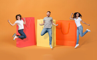 Naklejka premium Excited multiethnic millennials jumping by huge shopping bags