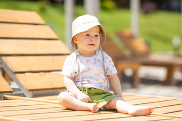 Cute baby boy is sitting on wooden beach chair near the sea during family vacation