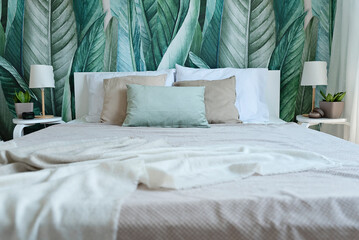 Bedrrom in cozy interior with modern design. Bed with pillows and green leaves on a wallpaper on the wall. 