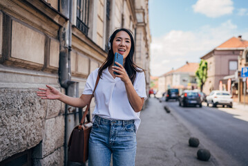 Japanese woman singing while listening music with headphones and mobile phone outside on the street