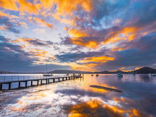 Fototapeta premium Aerial sunrise over the water with low cloud cover, boats and reflections