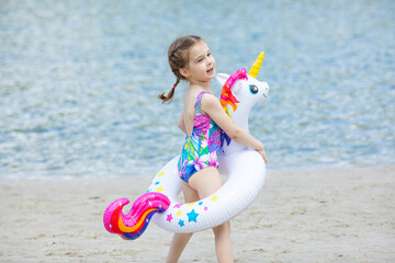 Side view adorable happy smiling little girl on beach vacation with swimming ring unicorn