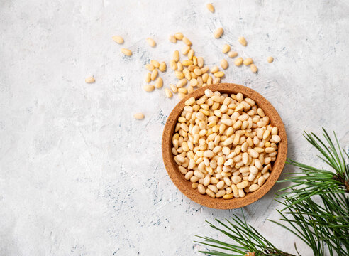 Pine nuts in a  wooden plate and scattered on a light texture background with branches of pine needles . The concept of a natural, organic and healthy superfood and snack.