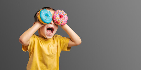 Happy cute boy is having fun played with donuts Bright photo of a child.