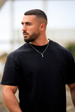 Hombre musculado con camiseta negra con inter&eacute;s en lo que pasa a su alrededor. Preocupaci&oacute;n, seriedad. Concepto de emociones y sensaciones.