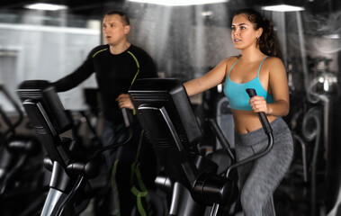 Fototapeta na wymiar Athletic young woman exercising on an elliptical trainer in the gym