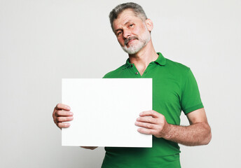 An aged attractive bearded man holds a sign in his hands and points at it with his finger. Presentation, advertising.