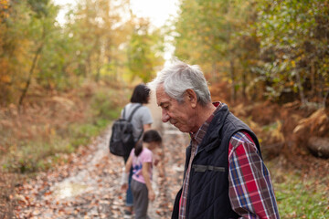 Fototapeta premium Grandfather with his grandson and granddaughter in the autumn forest, family hiking