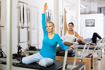 Active old woman stretching upper body practicing Pilates exercise in studio with elderly people