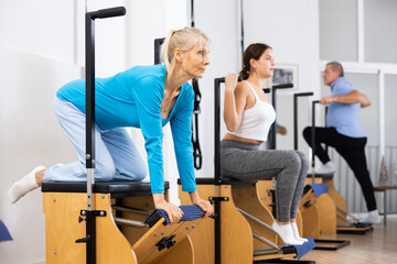 Focused mature woman performing stretching exercises while using pilates Wanda chair machine in fitness center