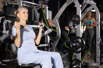 Fototapeta na wymiar Older sportswoman training at overhead press machine in gym