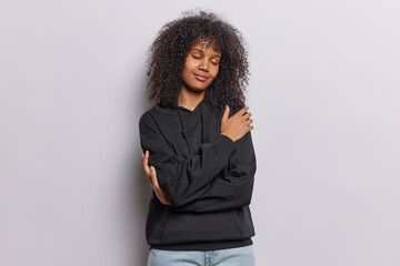 Tender curly haired African woman closes eyes embraces herself with pleasure feels comfortable...