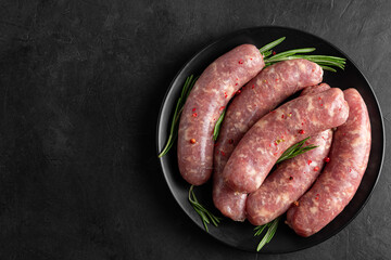 Raw sausages or bratwurst with spices and rosemary in a plate on black background. Top view - 614564163
