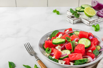Summer salad with watermelon, cucumber, cheese and mint in a plate on white table with fork. close up