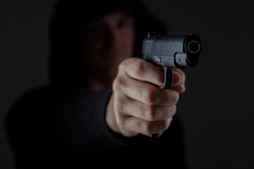 robber with gun aiming into camera. Man in hood threatens with firearm. Weapon in person's hands....