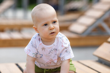 Cute baby boy is sitting on wooden beach chair near the sea during family vacation