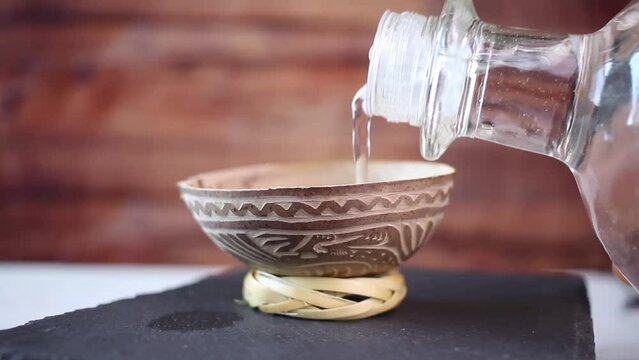 close shot of hand pouring mezcal or silver tequila into traditional glass, jicara