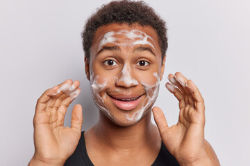 Handsome young African man revels in pure joy of cleansing his face with soap pleased with...