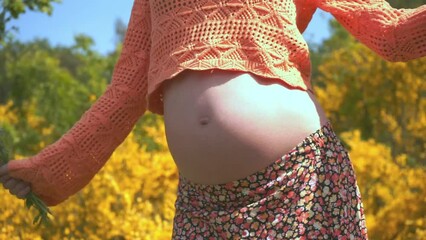 Active pregnancy.Close-up of naked belly of a pregnant woman whose happy dynamic dancing isolated on floral background at park.Cute Fun Mum Dancing.