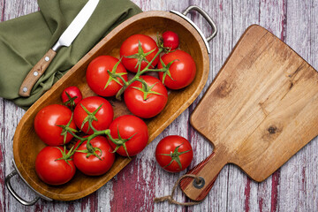 Fresh tomatoes in a wooden bowl and a cutting board with a knife on a wooden table. View from above. Place for text.