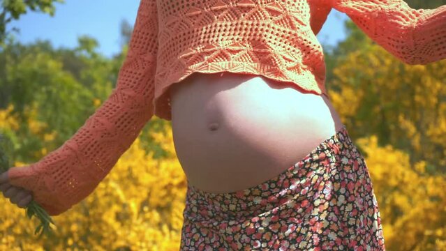 Active pregnancy.Close-up of naked belly of a pregnant woman whose happy dynamic dancing isolated on floral background at park.Cute Fun Mum Dancing.