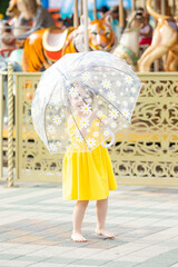 Happy little girl with an umbrella has fun in the amusement park at summer. Happy childhood concept.