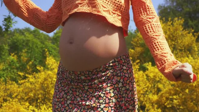 Active pregnancy.Close-up of naked belly of a pregnant woman whose happy dynamic dancing isolated on floral background at park.Cute Fun Mum Dancing.
