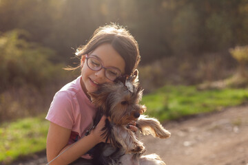 Little girl with her Yorkshire Terrier dog in a park at sunset