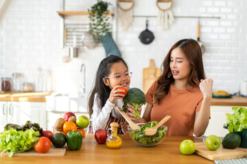 Portrait of enjoy happy love asian family mother and little asian girl daughter child having fun help cooking food healthy eat together with fresh vegetable salad and ingredient in kitchen