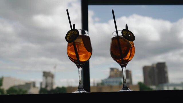 Two glasses with a beautiful cocktail are on the bar by the window