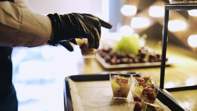 A waiter in gloves prepares canapes to treat people. A buffet is being prepared. Close-up of the waiter's hands