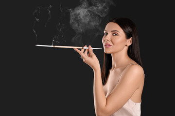 Fototapeta premium Woman using long cigarette holder for smoking on black background