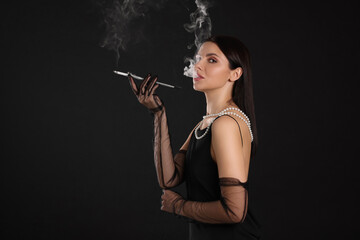 Woman using long cigarette holder for smoking on black background, space for text
